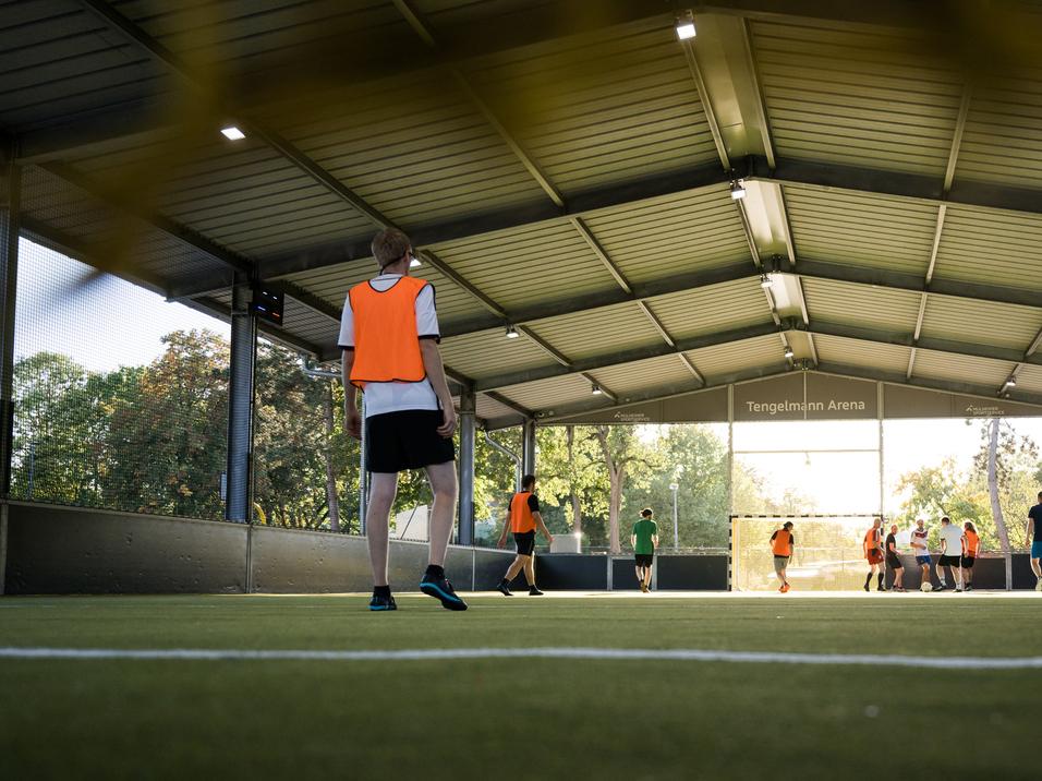 Gruppe von Jugendlichen in orangefarbener Spielformation auf einem Soccerfeld in der Tengelmann Arena.