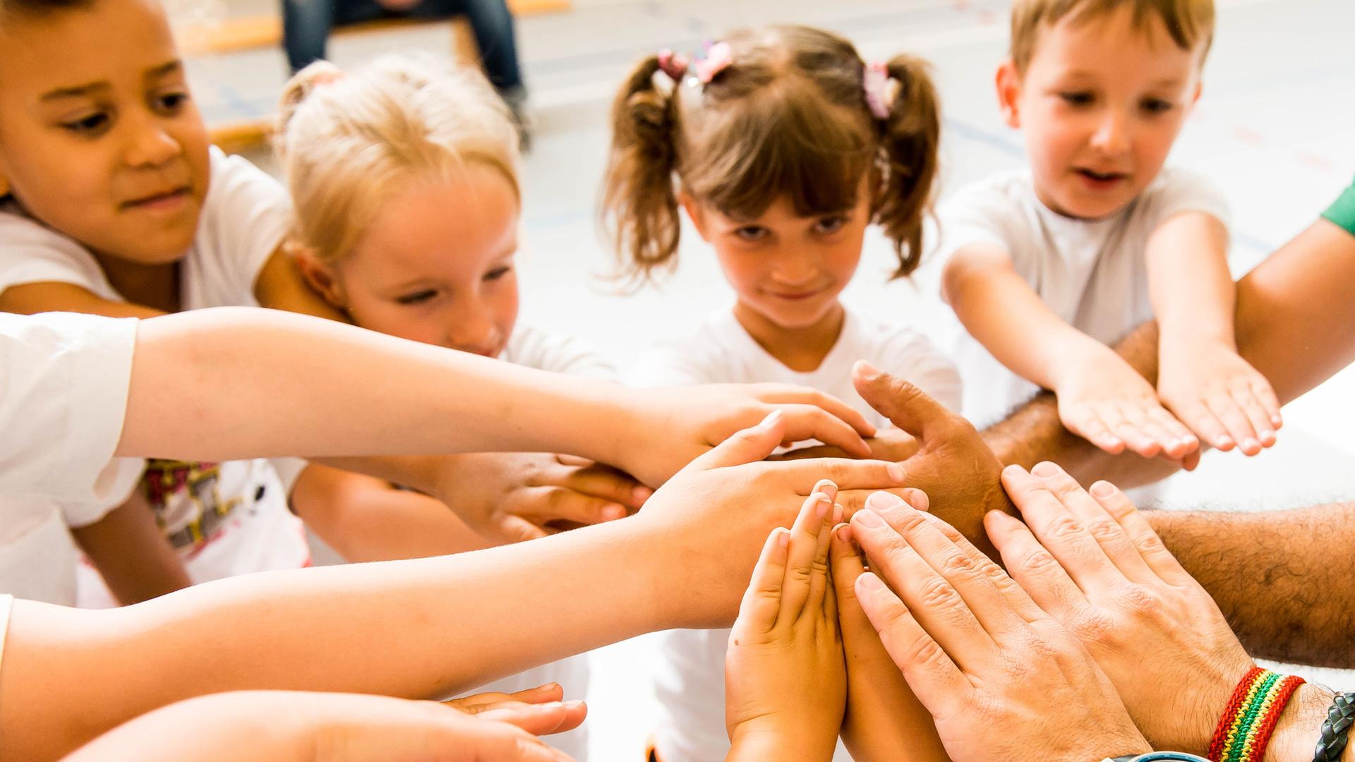 Kinder und Erwachsene legen ihre Hände in einem Kreis zusammen, symbolisieren Zusammenarbeit und Gemeinschaft.
