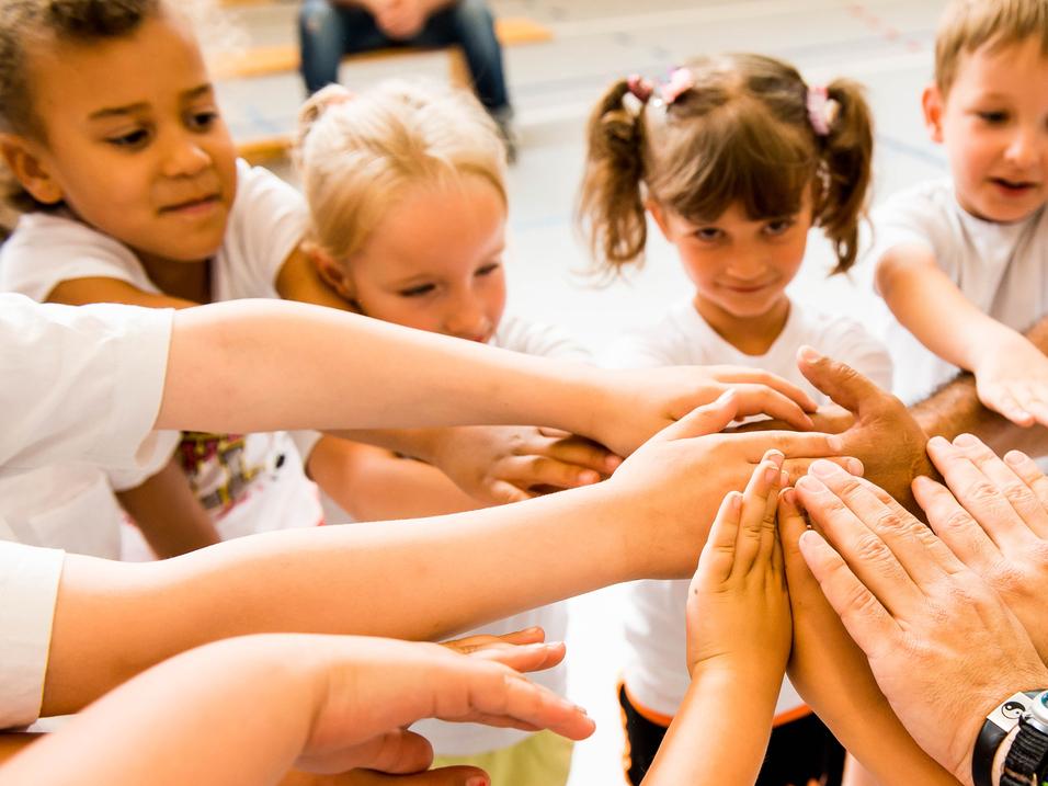 Kinder und Erwachsene legen ihre Hände in einem Kreis zusammen, symbolisieren Zusammenarbeit und Gemeinschaft.